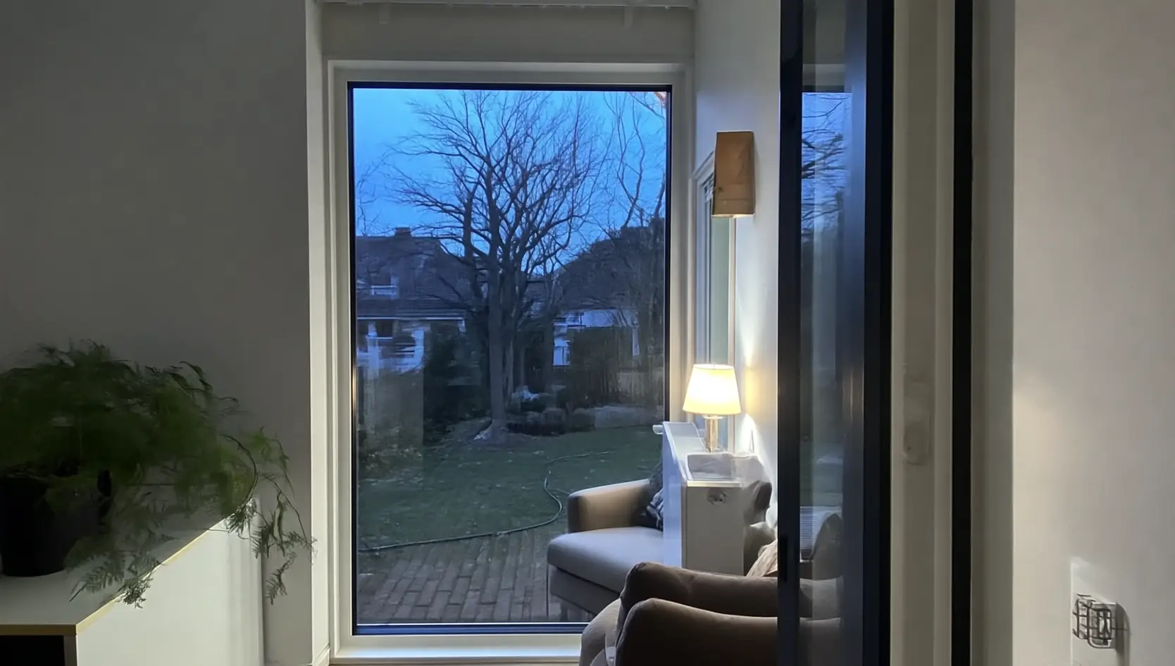 Hoog vast raam naast een zithoek, met zicht op een tuin bij schemer