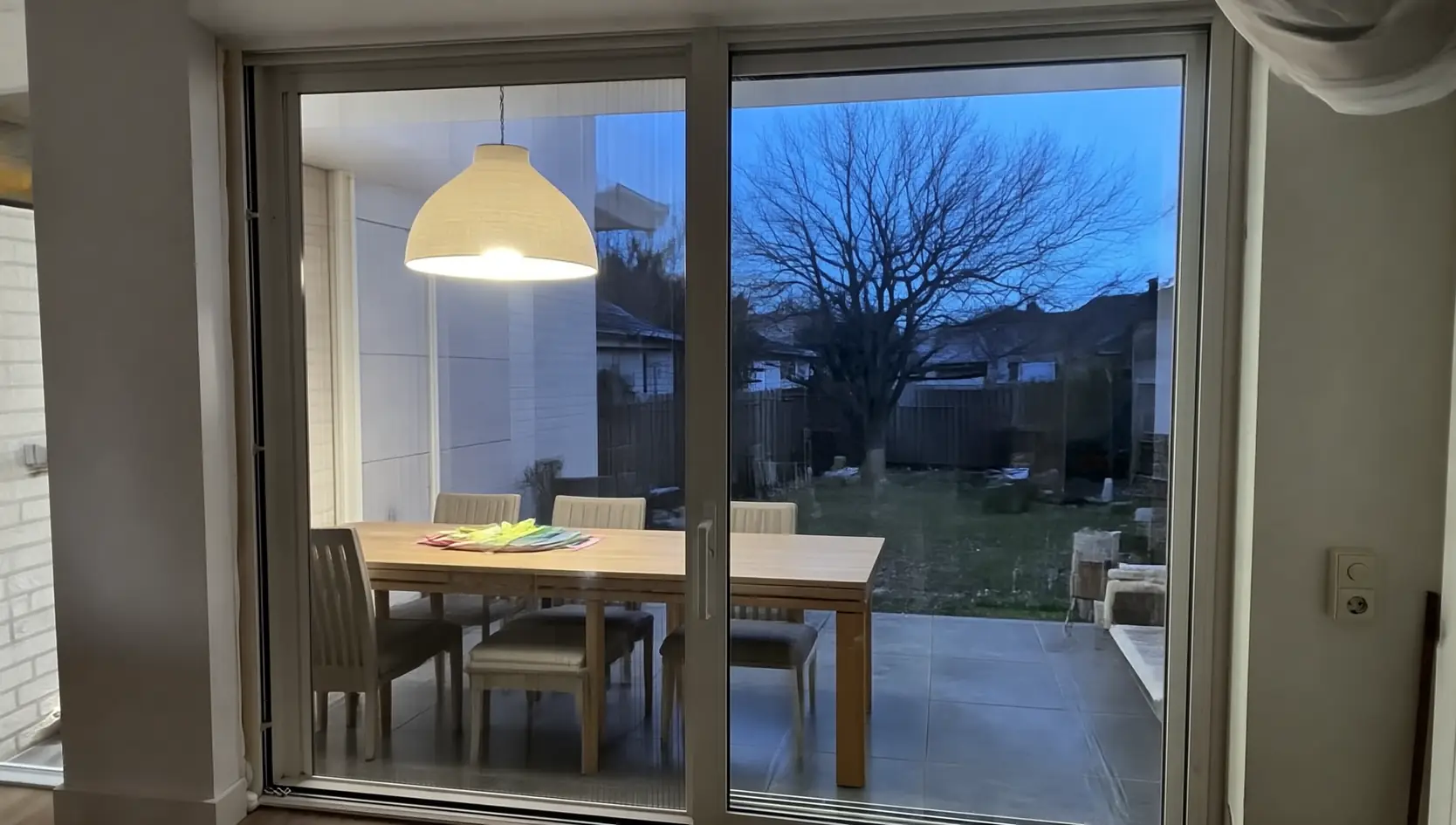 Crèmekleurige schuifpui met hordeur, gezien vanuit een eetkamer