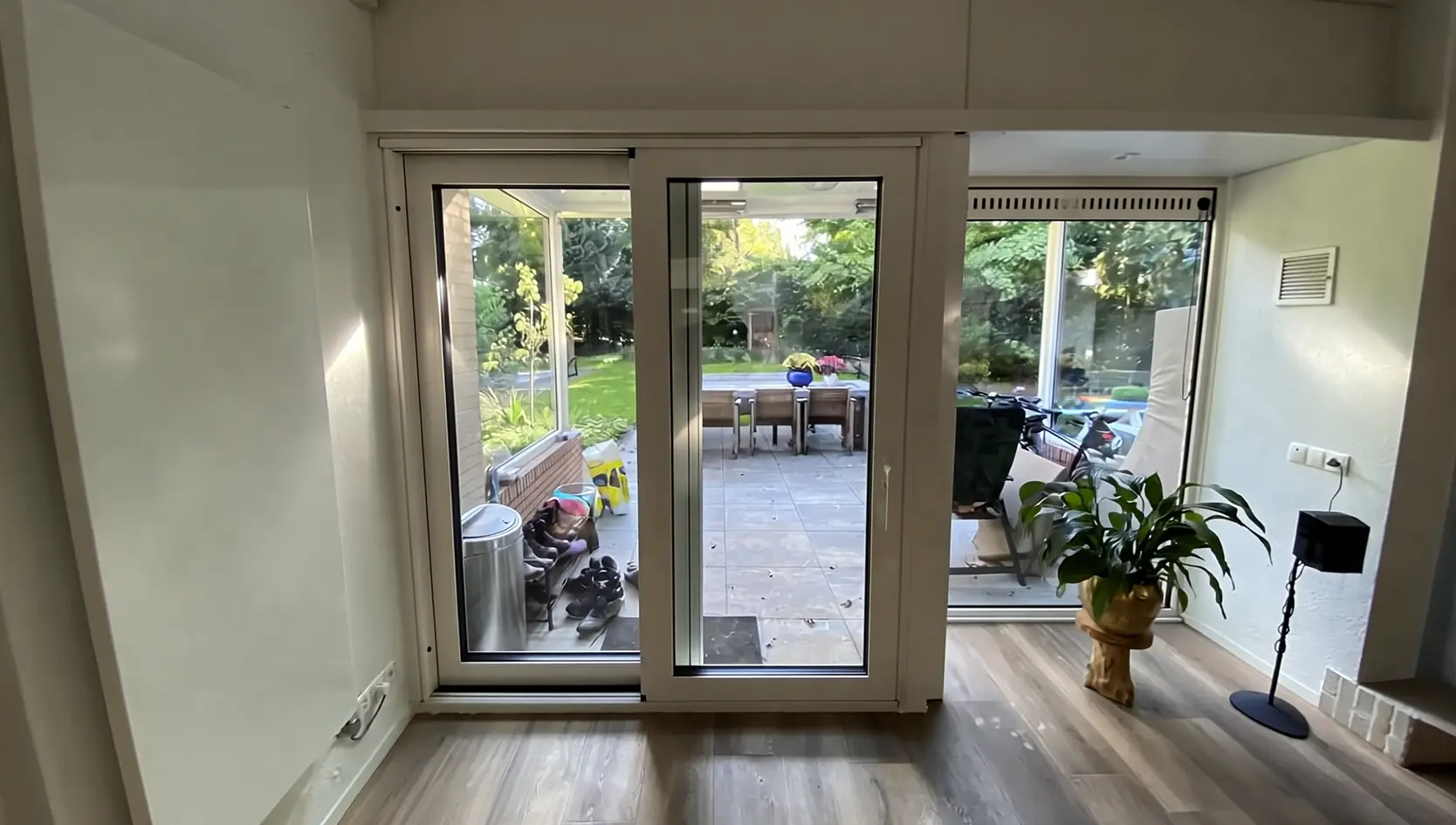 Crèmekleurige schuifpui met zijraam in een woonkamer, met zicht op een terras